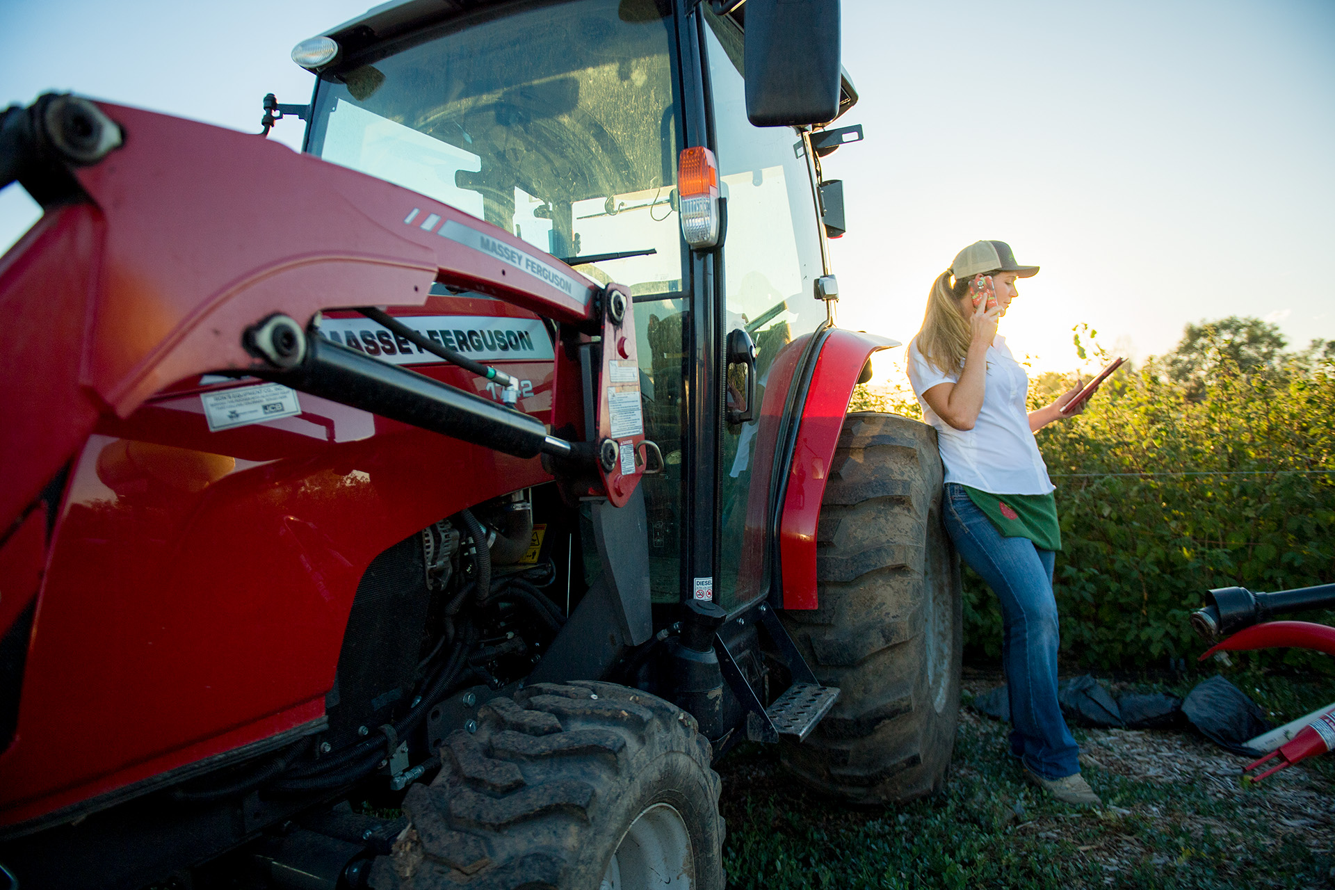 A woman leans against a red tractor while talking on the phone