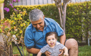 A man sits with his grandchild in a garden.