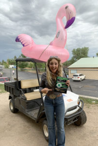 Young woman holds award and stands in front of golf cart with an inflatable flamingo strapped to the top
