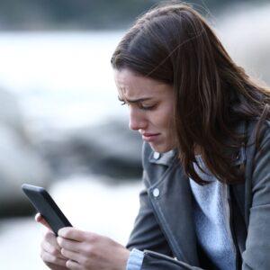 An upset young woman looks at her phone