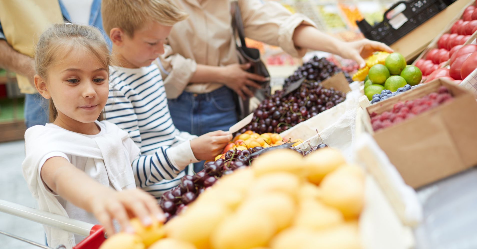 children reach for fruit at a market stand