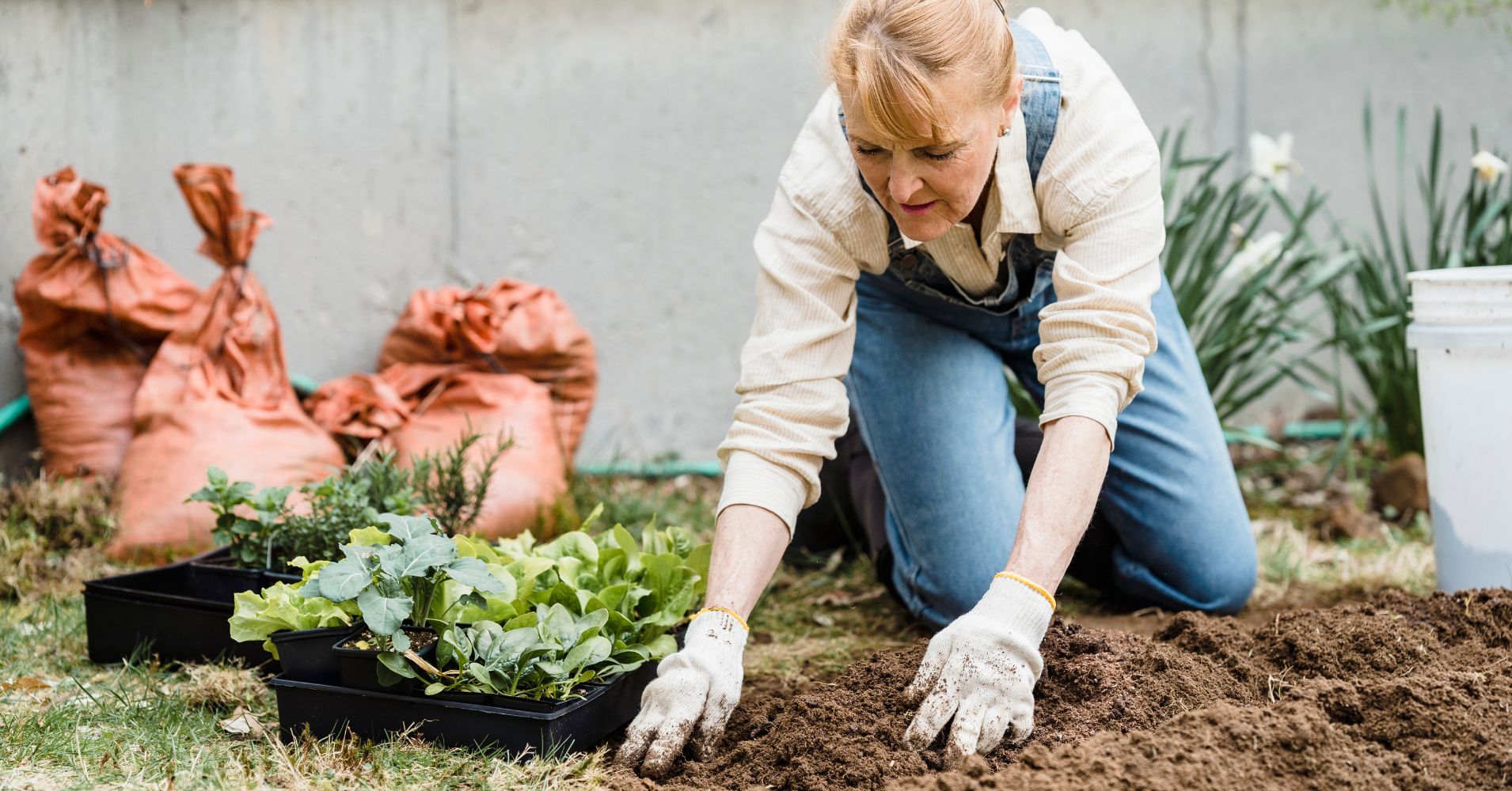 A woman kneels in the dirt preparing to plant green vegetable starts