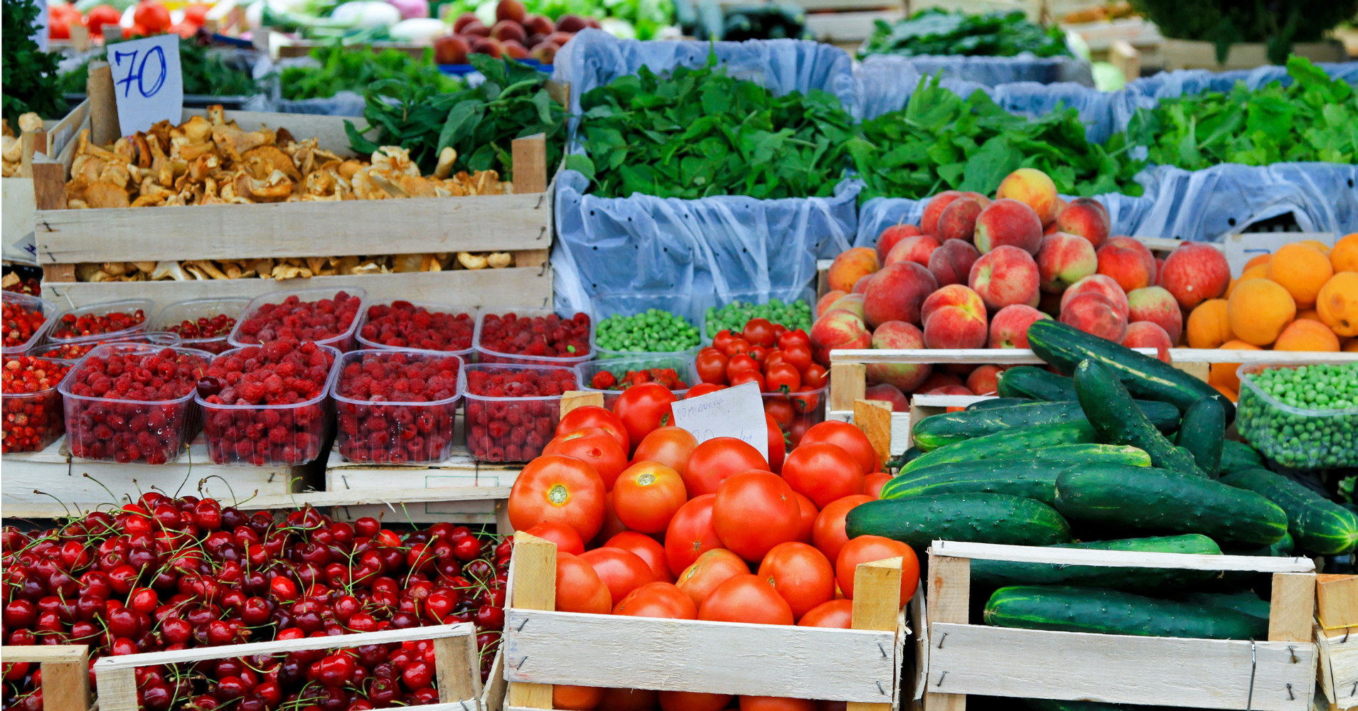 A farm stand with tomatoes, cucumbers, cherries and more produce.