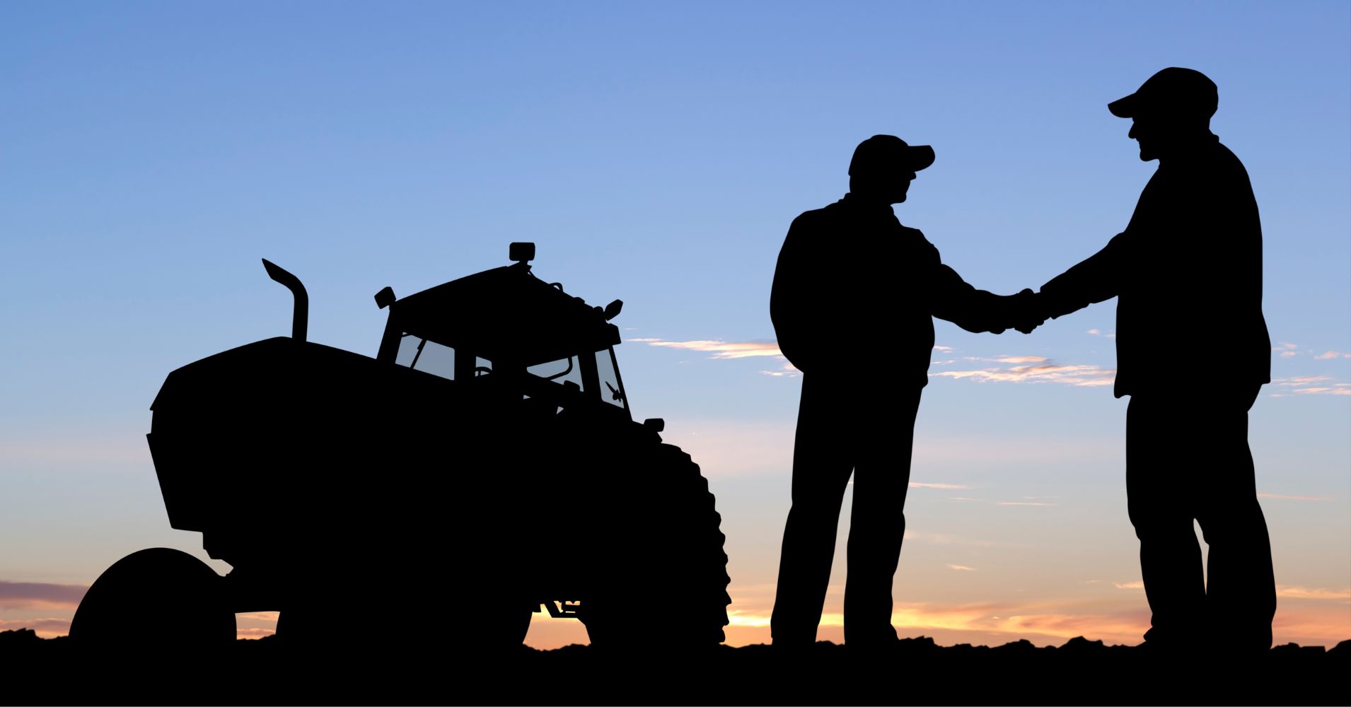 Two farmers shake hands, silhouetted alongside a tractor and illuminated by the sky at sunset