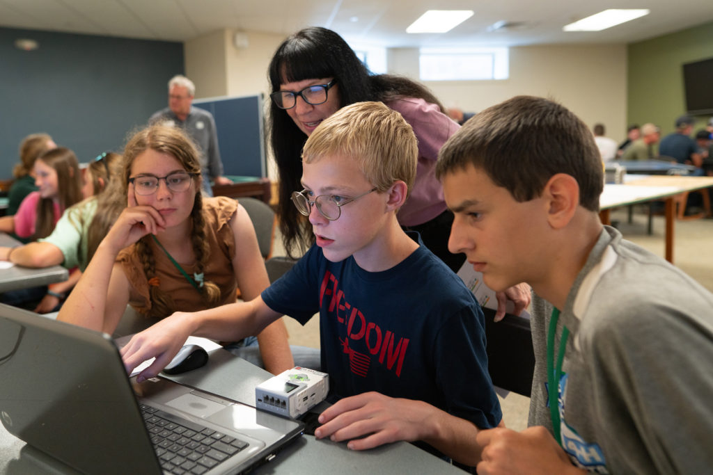 Three young people look at computer screen while teacher watches from behind them