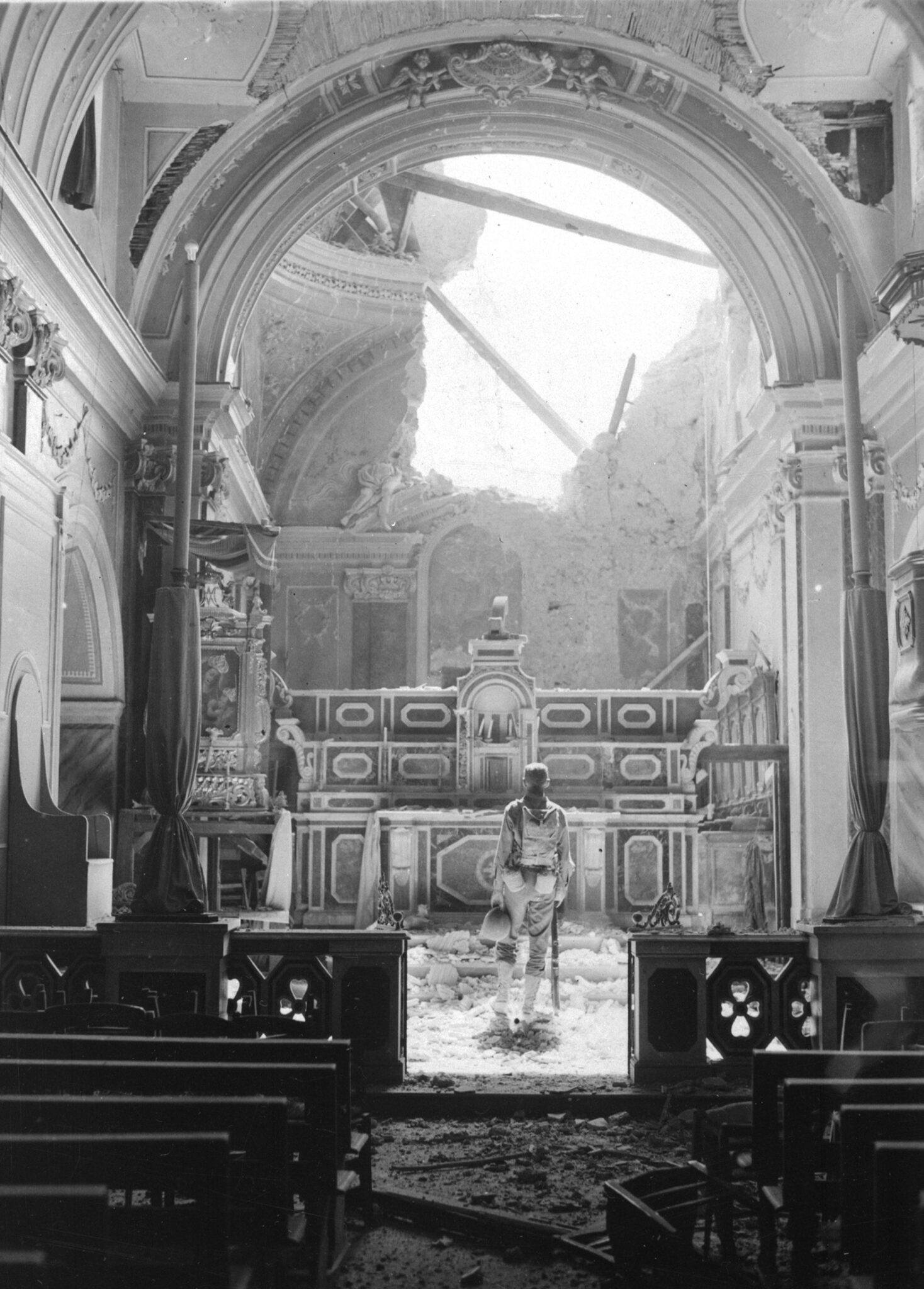 Private Paul Oglesby, 30th Infantry, standing in reverence before an altar in a damaged Catholic Church