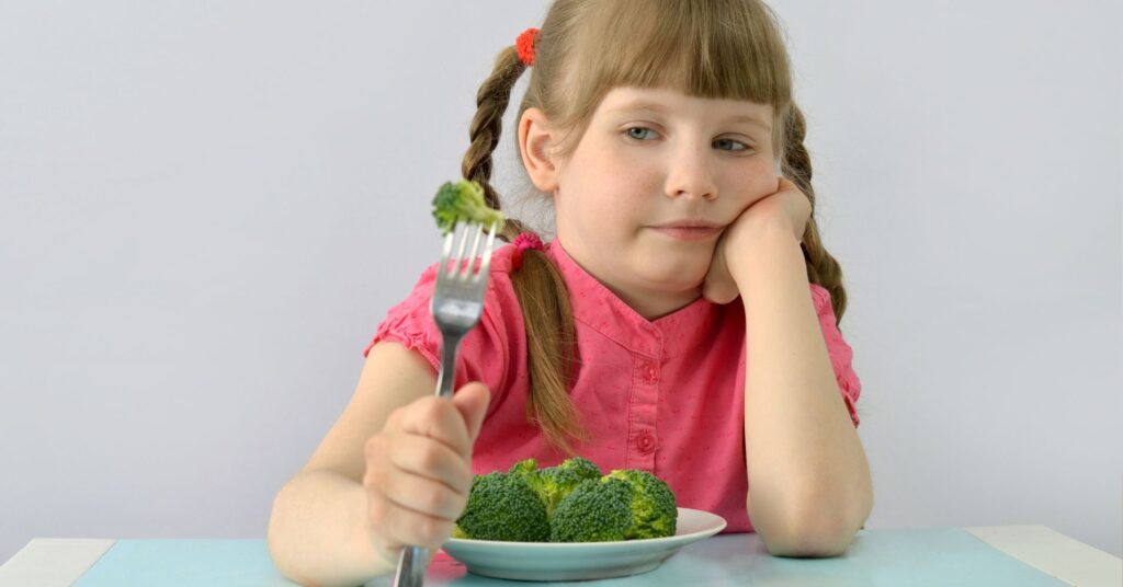 a kid looks skeptically at a broccoli floret on a fork